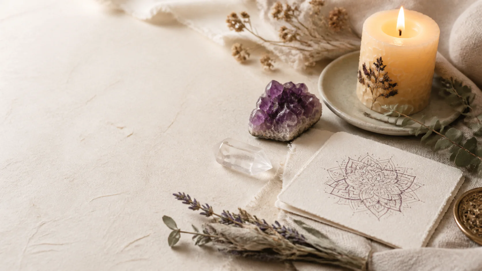 A candle, amethyst, quartz, dried botanicals, and a hand-drawn mandala on ivory paper