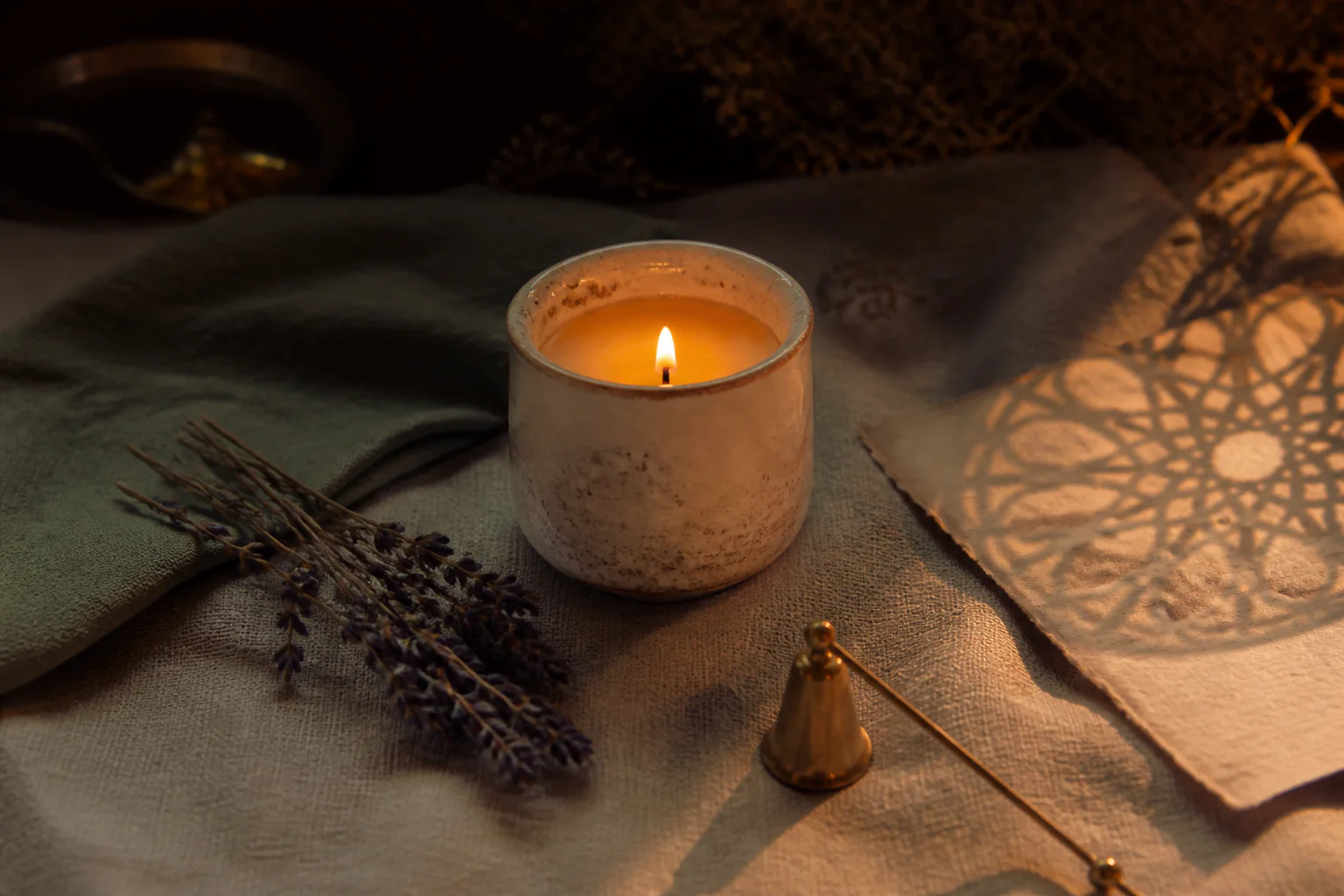 A glowing handmade candle with lavender, sage linen, and a mandala shadow